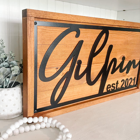 Wooden sign with last name on a decorative surface with plants and beads.