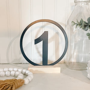Decorative table number '1' on a wooden stand with a neutral background