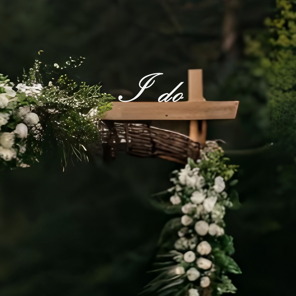 Wooden cross with floral decorations and 'I do' inscription against a dark background