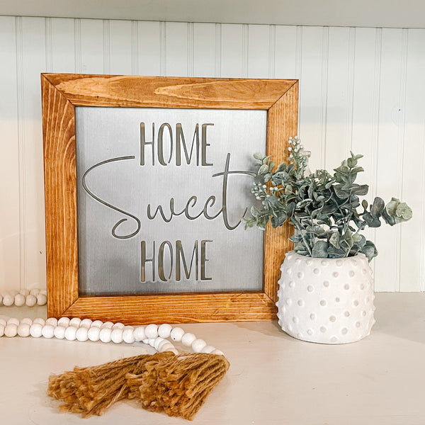 Decorative sign with 'Home Sweet Home' on a shelf with a plant and decor items.