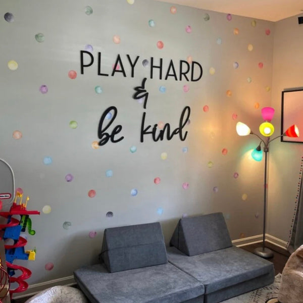 Children's room with 'Play Hard & Be Kind' wall quote, colorful polka dots, and gray sofa.